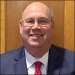 Image of John Manth, Board Chair, smiling in a suit with a red tie