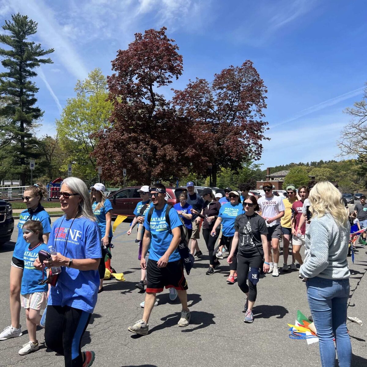 dozens of walk participants on a path in a park on a sunny, clear day