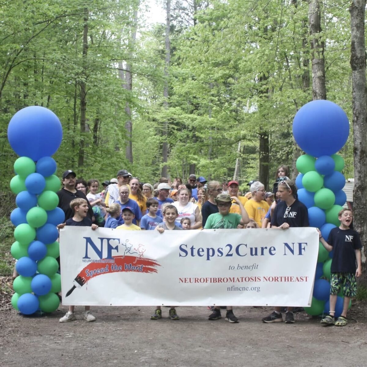 group of walkers holding Steps2Cure NF banner in a forest between two balloon pillars