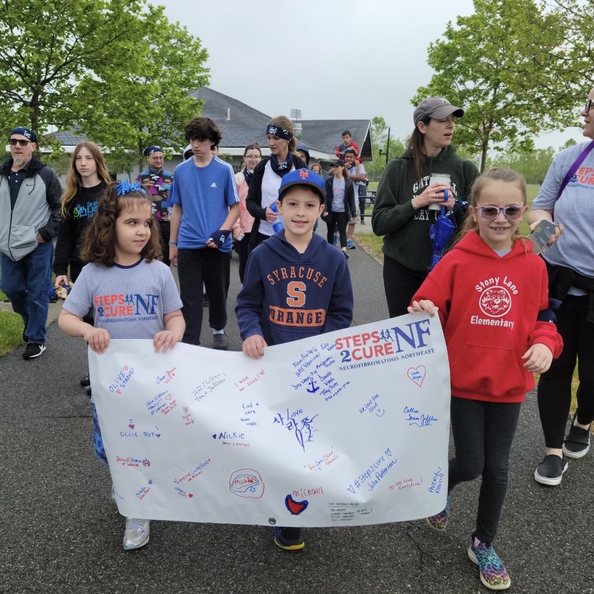 three children in front of a group of walkers, holding a Steps2Cure NF banner with signatures
