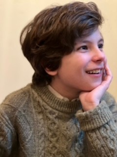 Young boy in brown sweater smiling and looking into the distance
