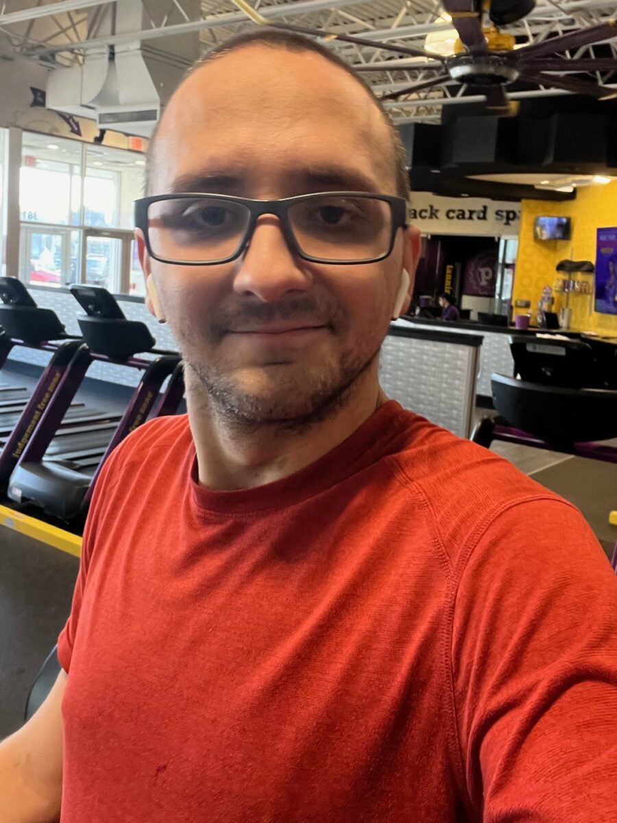 Man with short facial hair in a red shirt and glasses smiling with closed lips