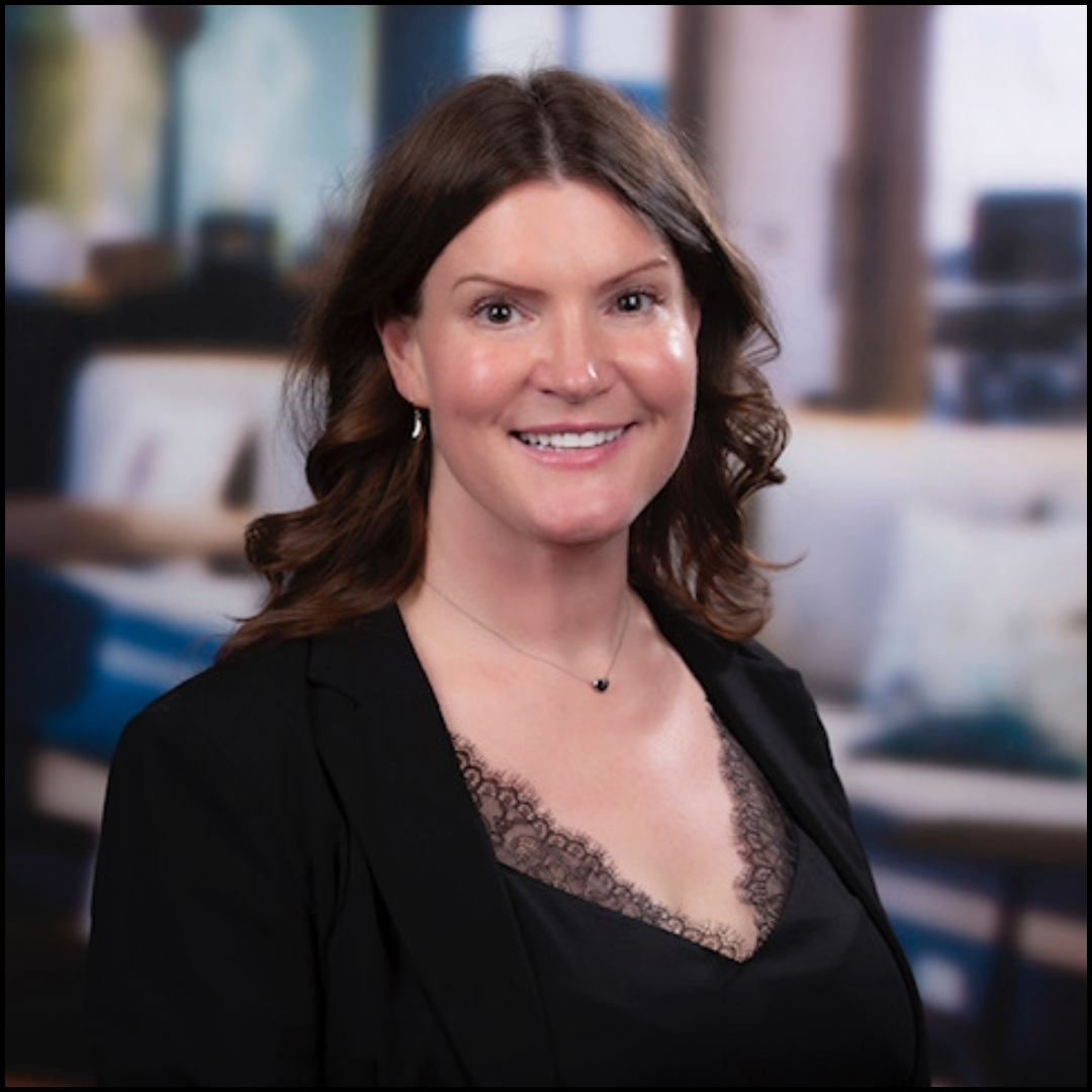 professional headshot of brunette woman wearing a black top and blazer, with an office scene in the background